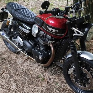 May include: A red Triumph motorcycle with a black leather seat and a silver front fender. The motorcycle has a black exhaust pipe and a black and silver engine.