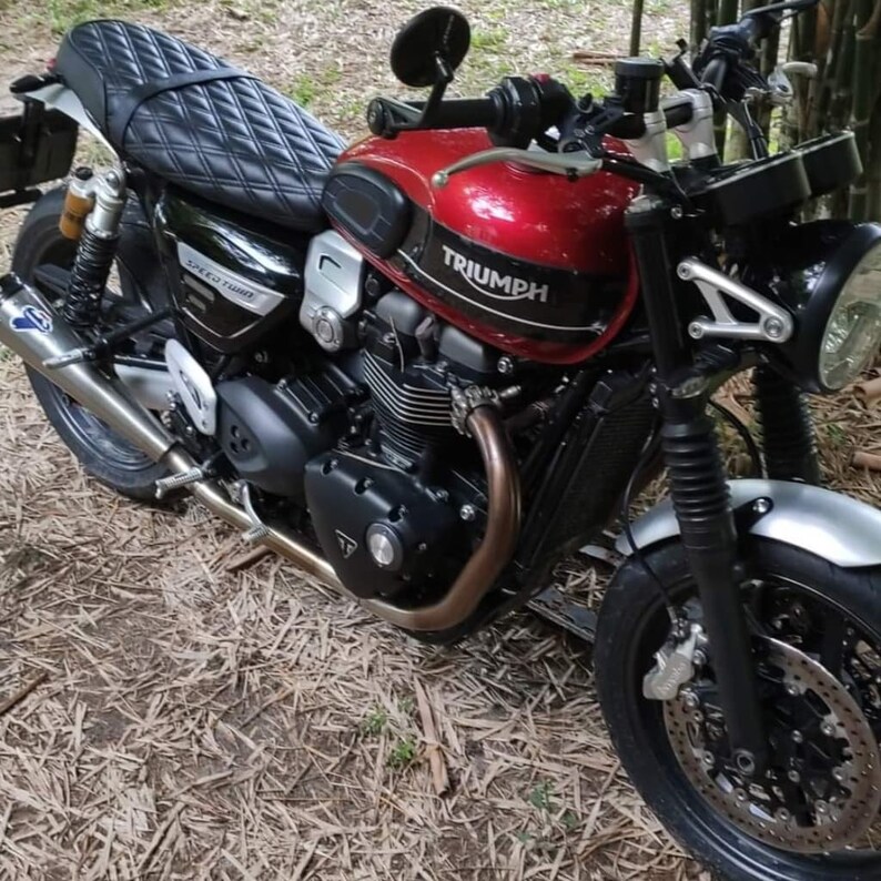 May include: A red Triumph motorcycle with a black leather seat and a silver front fender. The motorcycle has a black exhaust pipe and a black and silver engine.