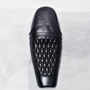 May include: Black motorcycle seat with a diamond-stitched pattern and a Union Jack design. The seat is made of leather and has a sleek, modern design. The seat is designed to fit a motorcycle.