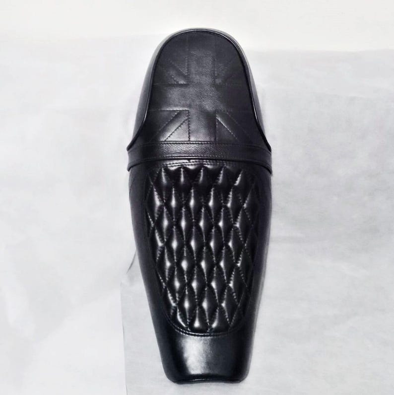 May include: Black motorcycle seat with a diamond-stitched pattern and a Union Jack design. The seat is made of leather and has a sleek, modern design. The seat is designed to fit a motorcycle.