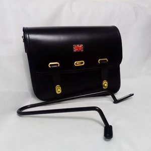 May include: Black leather motorcycle saddlebag with gold buckles and a small Union Jack flag on the front. The bag is attached to a black metal rack.