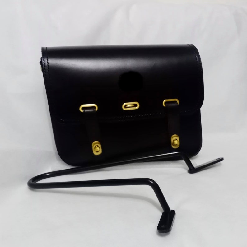 May include: Black leather motorcycle saddlebag with gold hardware and a black metal mounting bracket.