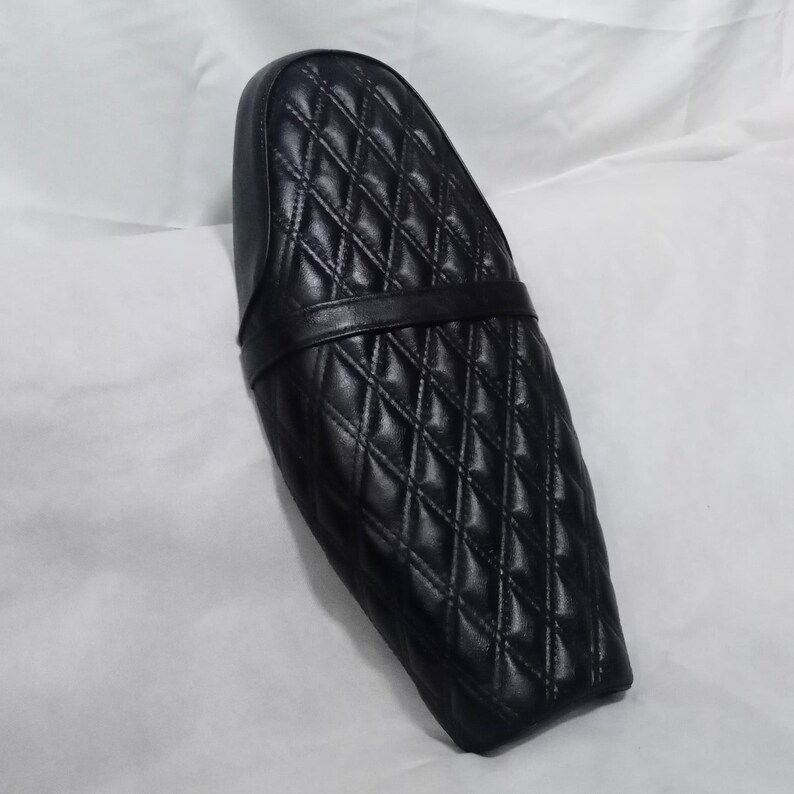May include: Black quilted motorcycle seat with a diamond pattern and a black leather strap.