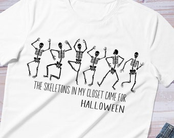 May include: White t-shirt with a black graphic of skeletons dancing and the text "The skeletons in my closet came for Halloween."