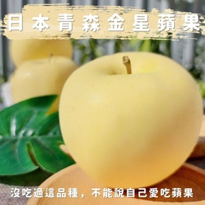 Puede incluir: Primer plano de una manzana amarilla con el texto "Japanese Golden Star Fruit" en el fondo. La manzana está sobre una superficie de madera con una hoja verde.