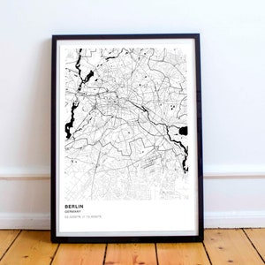 May include: Black and white map print of Berlin, Germany, in a black frame. The map shows the city's streets and waterways. The text "BERLIN, GERMANY, 52.5200° N, 13.4050° E" is printed below the map.