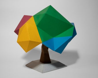 Op de afbeelding: Een kleurrijk papierkunst-boombeeld met een groen, blauw, geel en rood geometrisch bladerdak en een bruine papieren stam. De boom staat op een witte papieren basis.