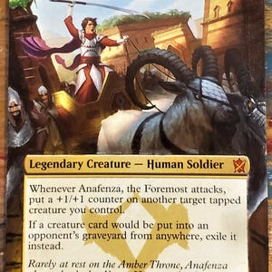 May include: A fantasy trading card depicting a legendary creature named Anafenza, the Foremost. The illustration shows a woman riding a chariot drawn by two goats. The card text reads "Whenever Anafenza, the Foremost attacks, put a +1/+1 counter on another target tapped creature you control. If a creature card would be put into an opponent's graveyard from anywhere, exile it instead. Rarely at rest on the Amber Throne, Anafenza always leads the Abzan Houses to battle." The card has a power and toughness of 4/4.