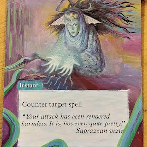 May include: A blue and purple magic card with a woman in a blue robe holding her hands out, surrounded by white bubbles. The card text reads "Counterspell" and "Counter target spell."  "Your attack has been rendered harmless. It is, however, quite pretty." -Saprazzan vizie