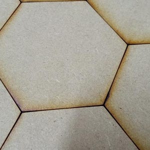 May include: A series of light tan, flat, hexagonal tiles arranged in a repeating pattern. Each tile features smooth, matte surfaces with distinct, dark brown, laser-cut edges that create a clear, defined border between the individual shapes.
