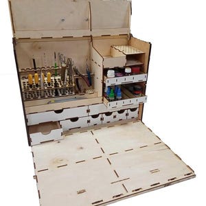 May include: A wooden craft organiser with multiple compartments, drawers, and tool holders. The organiser is open, revealing various tools, paint bottles, and storage spaces. The natural wood finish gives it a clean, organised look, perfect for hobbyists.