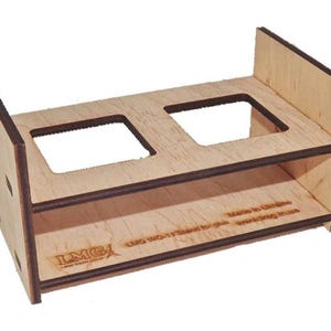 Könnte beinhalten: Ein heller Holzständer mit zwei quadratischen Ausschnitten auf der oberen Ablage. Die Seitenwände sind hoch und die Basis ist mit einer Lasergravur versehen, die LMG, LMG WO-17 Stand for glue und Made in Ukraine lautet.