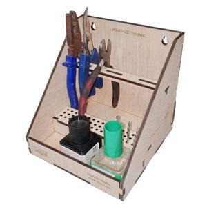 Könnte beinhalten: Ein Werkzeug-Organizer aus hellem Holz mit einer schrägen Rückwand mit Schlitzen für Zangen, einem mittleren Regal mit zahlreichen kleinen runden Löchern für Bohrer und einem Bodenbereich, der zwei quadratische Flaschen mit schwarzen und grünen Kappen enthält.