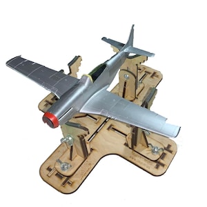 Könnte beinhalten: Ein silbernes Modellflugzeug mit roter Nase steht auf einem Holzständer. Das Flugzeug hat detaillierte Flügel und ein Cockpit. Der Ständer ist aus hellem Holz gefertigt und verfügt über verstellbare Halterungen.