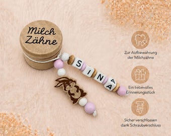 May include: A wooden baby tooth keepsake box with the words "Milch Zähne" printed on the lid. A beaded pacifier clip with the name "SINA" and a brown bunny charm is attached. The clip features white, pink, and wooden beads.