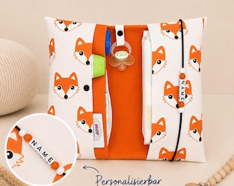 May include: A white and orange baby changing clutch with a repeating fox face pattern. The clutch has an orange interior and holds a bottle, diapers, and a pacifier. A beaded name tag is attached.