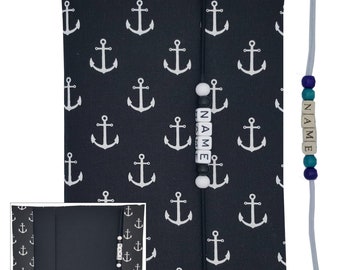 May include: A black fabric notebook cover with a white anchor pattern. The cover has a white string with white beads that spell "NAME". A separate white string with blue and turquoise beads also spells "NAME".