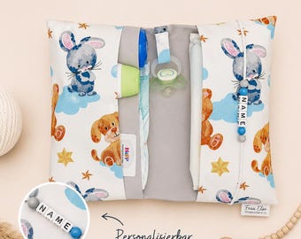 May include: A white and gray baby changing pad with a pattern of bunnies, teddy bears, and puppies. The pad has pockets for essentials and a pacifier clip. The text "Personalizierbar" is visible.