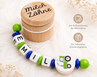 May include: A wooden keepsake box with the text "Milch Zähne" and a beaded pacifier clip. The clip features white lettered beads spelling a name, green and blue beads, and a wooden tractor design. The box is for baby teeth.