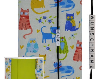 May include: A white fabric book cover with a colorful cat pattern. The cover has a black ribbon bookmark with the word "NAME" on it. The cover also has a black ribbon with the word "WUNSCHNAME" on it.