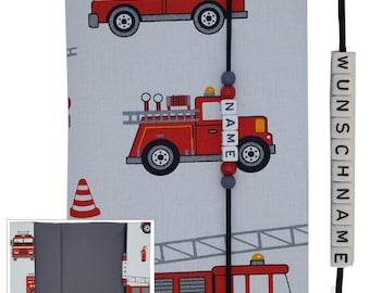 May include: A gray fabric photo album with a red fire truck design. The album has a black ribbon closure and a personalized name tag that reads "NAME". The album also has a black bookmark with the word "WUNSCHNAME" on it.
