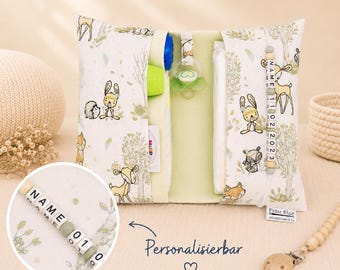 May include: A white and green baby organizer with a woodland animal print, featuring a pacifier, a bottle, and a personalized name tag. The organizer is open, revealing pockets and compartments for baby essentials.