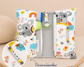May include: A white and gray baby changing pad with a koala bear and rainbow pattern. The pad has a gray interior and holds a pacifier, bottle, and diapers. A beaded name tag is attached. The text "Personalizable" is also visible.