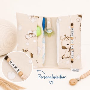 Könnte beinhalten: Beige Wickelunterlage mit Giraffenillustration und Namensschild aus Perlen. Die Unterlage hat Taschen für Windeln, einen Schnuller und andere Babyutensilien. Der Text "Personalisierbar" ist ebenfalls sichtbar.