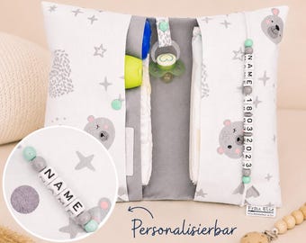 May include: A white and gray baby organizer pillow with a bear and star pattern. The pillow has pockets for baby essentials, including a pacifier, bottle, and diapers. A beaded name tag and the text "Personalizable" are visible.