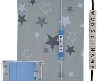 May include: A gray fabric book cover with a white string and blue beads that spell out the word "NAME". The cover has a pattern of white and gray stars. A black string with white beads that spell out the word "WUNSCHNAME" is on the right side of the image.