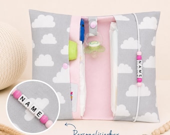 May include: A gray and pink baby changing clutch with a cloud pattern. The clutch is open, revealing a pacifier, diaper, and other baby essentials. A beaded name tag with the word "NAME" is attached. The text "Personalisierbar" is also visible.