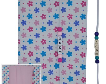 May include: A white fabric book cover with a pink and blue floral pattern. The cover has a white ribbon bookmark with pink and blue beads and the word "NAME" spelled out in white letters.