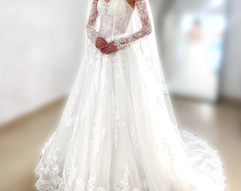 May include: A white strapless wedding dress featuring a sweetheart neckline, a corset-style bodice, and long sheer lace sleeves. The full-length skirt is adorned with intricate floral lace appliqués and a scalloped hem, paired with a long tulle veil.