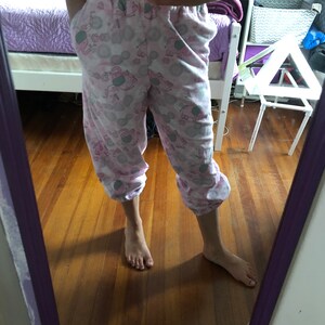 May include: Pink pyjama trousers with a pattern of elephants and flowers. The trousers have a drawstring waist and are cropped.