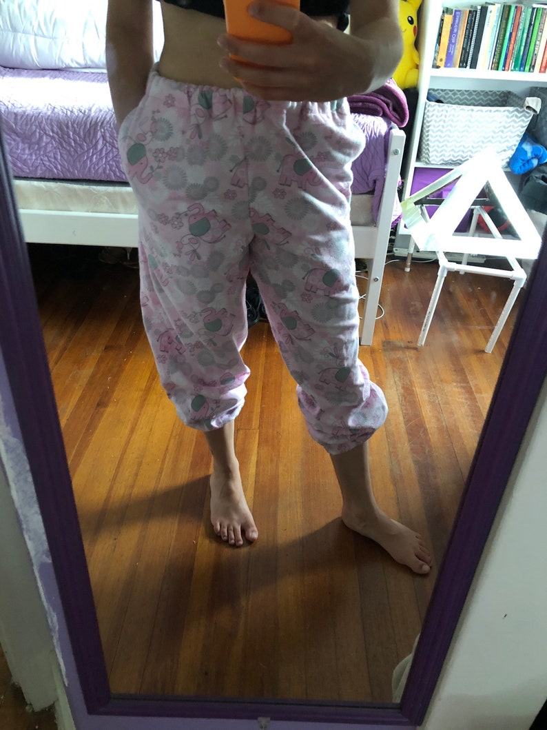 May include: Pink pyjama trousers with a pattern of elephants and flowers. The trousers have a drawstring waist and are cropped.