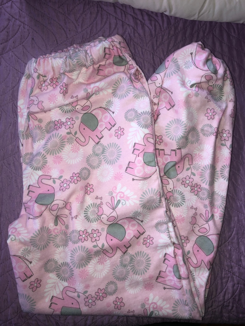 May include: Pink and grey patterned leggings with a design of elephants and birds. The leggings have an elasticated waistband.