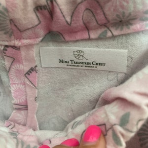 May include: A pink fabric with a white floral pattern and a white label that reads "Mina Treasures Chest Handmade by Romina D."