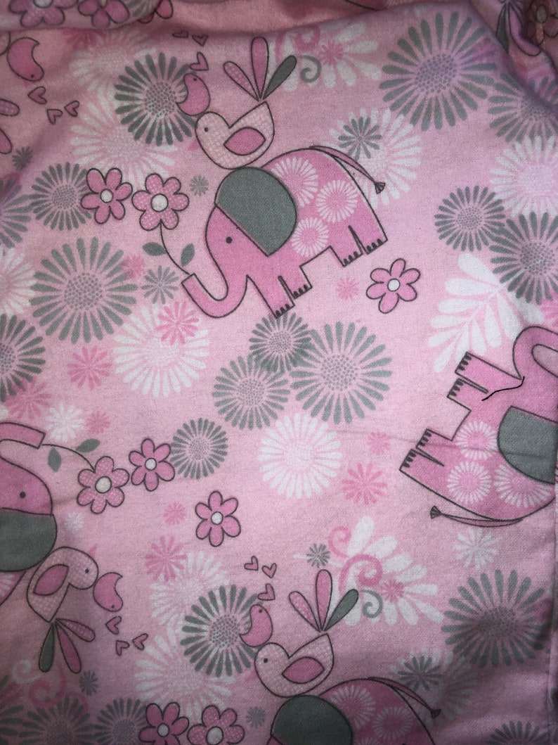 May include: Pink fabric with a repeating pattern of grey and white flowers, pink elephants, and pink birds. The birds have grey wings and beaks.