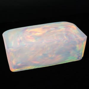May include: A rectangular, iridescent box with rounded edges. The box has a pearlescent, swirling pattern with hints of yellow, pink, and green. The box is set against a black background.