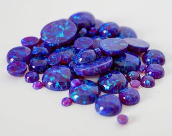 May include: A collection of polished opals in various shapes and sizes, showcasing a vibrant display of blue and purple hues with iridescent flashes. The opals are arranged on a white surface. The text "THEOPALDEALER" is at the bottom.