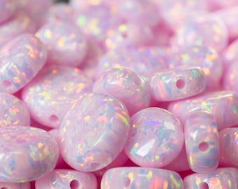 May include: Close-up of a collection of pink opal beads with iridescent flashes. The beads are in various shapes, including round, oval, and barrel, each with a drilled hole. The text "THEOPALDEALER" is at the bottom.