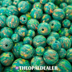 Puede incluir: Un primer plano de cuentas de ópalo de color verde azulado con patrones arremolinados de verde, naranja y amarillo. Las cuentas son redondas con un agujero en el centro. El texto "THEOPALDEALER" está en la parte inferior.