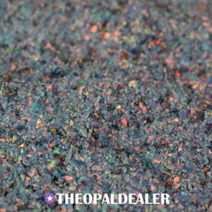 May include: A collection of small, crushed dark gray opal fragments featuring iridescent flashes of orange, green, and blue light. The text THEOPALDEALER is printed in white at the bottom center, accompanied by a small white star icon.