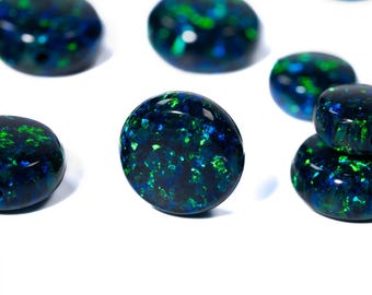 May include: A collection of polished, oval-shaped opals. The opals display a dark blue base color with vibrant green and blue flashes. The gemstones are arranged on a white background, showcasing their iridescent qualities.