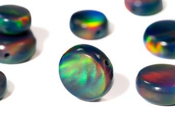 May include: A collection of iridescent black opal beads with a flat, disc-like shape. The beads display a play of color, with flashes of green, blue, and red. Each bead has a small hole for stringing. The background is plain white.