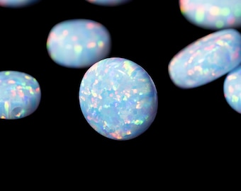 May include: A collection of oval and round opals with a milky blue base color and iridescent flashes of color. The opals are scattered against a black background, showcasing their unique internal patterns and textures. These gemstones are ideal for jewelry making.