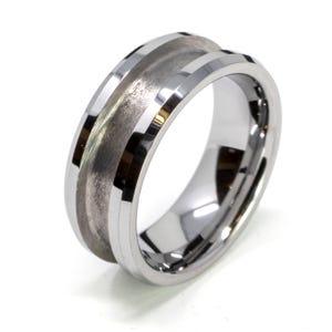 May include: A polished silver ring with a brushed metal center band. The ring has a wide band design with a smooth, reflective surface on the outer edges. The center band has a textured, matte finish.