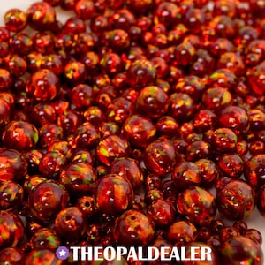 May include: A close-up of numerous round beads in varying sizes, displaying a mix of red, orange, and yellow hues. The beads have a glossy, polished appearance. The text "THEOPALDEALER" is visible at the bottom of the image.