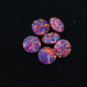 Op de afbeelding: Zes ronde, gefacetteerde edelstenen met een levendig, veelkleurig patroon van paars, oranje en groen. De edelstenen zijn geplaatst tegen een zwarte achtergrond, wat hun glans en kleurvariaties benadrukt. Ideaal voor het maken van sieraden.