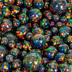 Puede incluir: Un conjunto de cuentas de ópalo azul oscuro iridiscentes con destellos de color vibrantes. Las cuentas varían en tamaño y tienen un acabado pulido y brillante. Cada cuenta está perforada con un agujero para ensartar, ideal para hacer joyas.
